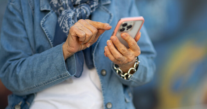 detail of elderly lady holding smartphone and tapping on screen with index finger