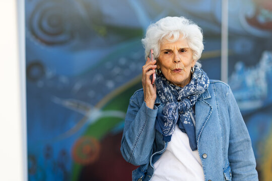 an elderly white-haired woman gossiping on her phone against a blurry blue patterned background