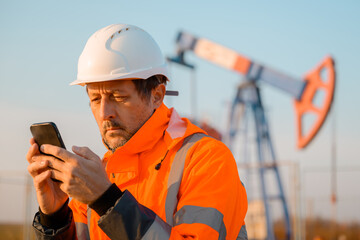 Drilling rig engineer using mobile phone while supervising the process of oil and gas, monitoring...
