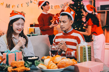 Group of happy Asian friends celebrating Christmas and decorate the Christmas tree indoors. Beauty woman with Christmas Gifts. New Year party. Woman hands decorate Christmas tree red ball, bauble.