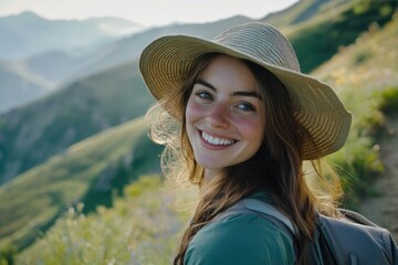 A smiling woman with a straw hat enjoys a hike through a mountain landscape.