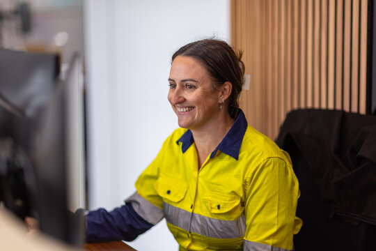 smiling adult woman in high visibility clothes working in front of her computer in an office.