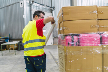 Warehouse worker wrapping pallet of boxes and luggage with plastic film