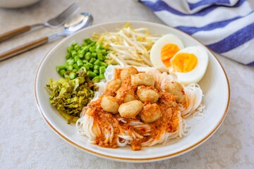 Kanomjeen namya krati ,Rice vermicelli with minced fishes and meatball and coconut milk in red curry on white plate side dish with boiled egg and vegetables