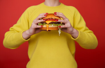 A person wearing a bright yellow sweater. holding a burger with juicy meat patty, lettuce, and a dripping sauce
