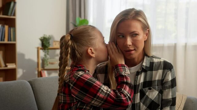 Mischievous Caucasian girl child whispering secret in ear female mother mom shocked surprised woman listen little daughter gossip telling interesting story rumor kid speak with parent at home family