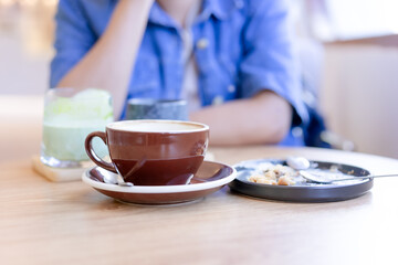 Focus on coffee mug and empty plate with bits of pastry and spoon in the plate. placed on the table On a blurry background, a woman sits with her hands on her chin. In the cafe, the atmosphere is warm