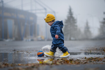 Happy toddler walks through the puddles in blue jumpsuit with splashes close-up and copy space.