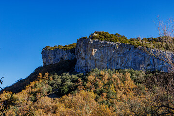 A dramatic rocky cliff surrounded by a vibrant autumn forest under a deep blue sky, capturing the beauty of nature in northern Spain.
