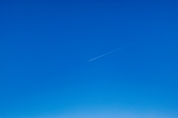 A minimalistic image of a white airplane contrail streaking across a deep blue sky, symbolizing...