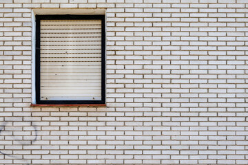 A minimalistic design of a white brick wall featuring a single closed window with shutters, creating a clean and geometric aesthetic.