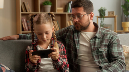 Worried upset Caucasian dad man male daddy touching speak little girl child daughter family problem at home bad behavior kid ignore father guy playing online game mobile phone device gadget addiction