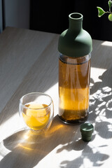 Cold brew tea in a glass bottle, accompanied by a clear glass, placed on a table.