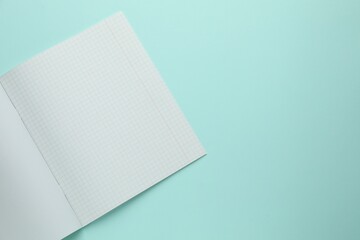 Open copybook with checkered sheets of paper on light blue background, top view. School stationery