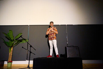 Male performer delivering a monologue on stage in a dimly lit theater with audience