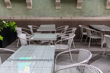 A patio with many chairs and tables, some of which are empty. The chairs are made of wicker and the tables are made of glass. The patio is outside and has a nice view