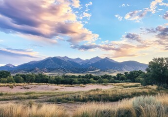 Scenic View of Majestic Mountain Range Under Soft Clouds at Sunset with Vibrant Sky and Golden Grasslands in the Foreground, Capturing the Beauty of Nature