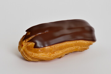 A chocolate covered pastry on a white background. A eclair with a gray background and chocolate. Chocolate eclair gray background cake dark lies. A cake with a dark lifestyle chocolate eclair lying.
