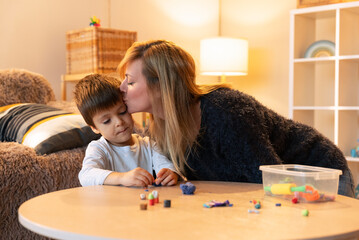 Loving mother kissing her son while playing with clay at home
