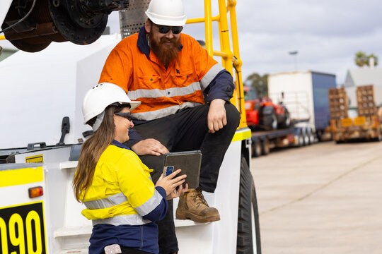 Two workers wearing high visibility clothing man sitting on the truck while woman showing the tablet