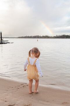 toddler girl playing on shore of tidal river in Port Macquarie with rainbow in sky