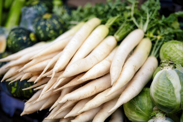 Close-up of white radishes with leafy tops on display at a local market, representing fresh and organic produce for cooking and salads.