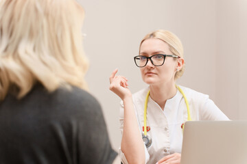 A confident female doctor wearing a stethoscope and glasses attentively listens to a patient during...
