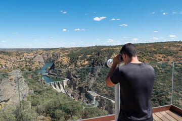Jovem turista a observar com os binóculos a barragem de Castro a partir do miradouro de Penha das...