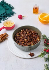 Prepared raisins with spices, strong alcohol and candied lemon peels for Christmas baking in a green bowl on a white concrete background. Merry Christmas concept.