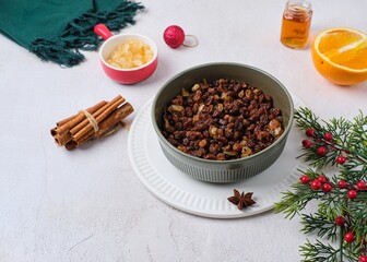 Prepared raisins with spices, strong alcohol and candied lemon peels for Christmas baking in a green bowl on a white concrete background. Merry Christmas concept.