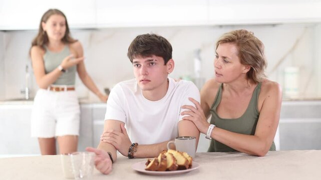 Woman sits near guy and comforts him during quarrel with girl. Mother soothe and calms upset guy takes side of son in altercation with sister. Young woman is outraged by guy behavior and blames