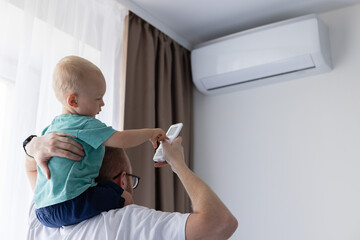 Father and little son turn on air conditioner using remote control.
