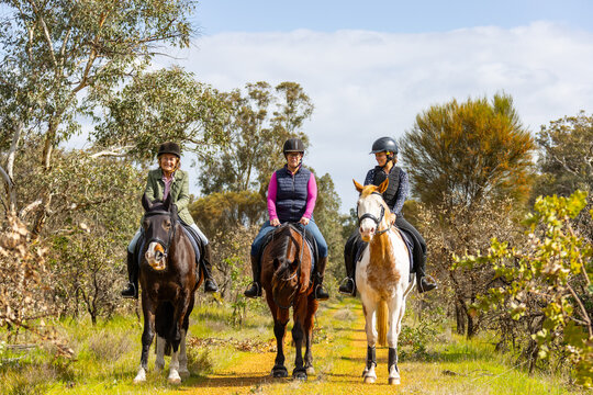 Multi-generation women riding horses along a narrow dirt path.