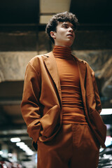 Stylish young man in an orange outfit standing confidently in a modern underground setting