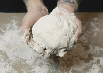 Tattooed hands holding fresh dough.