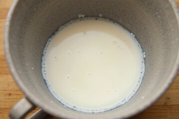 Leftover fresh milk in a cup gone bad and stale, becomes thicken and harden, the casein protein coagulated and curdle. Spoiled milk in glass undergone solidification forming solid curds. Closeup view.