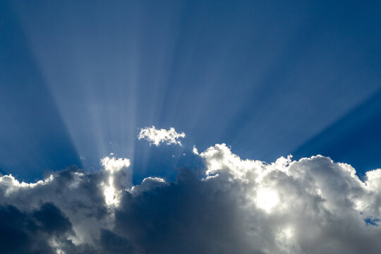 Crepuscular rays, or God beams, emerging from behind white flufy clouds