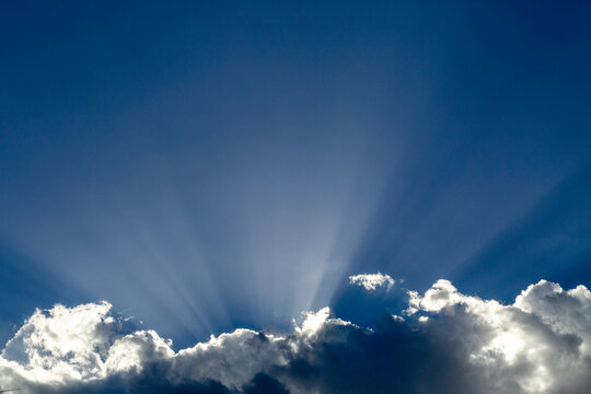 Crepuscular rays, or God beams, emerging from behind white flufy clouds