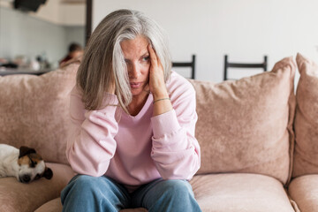 Sad pensive middle age woman looking down depressed sitting on the sofa