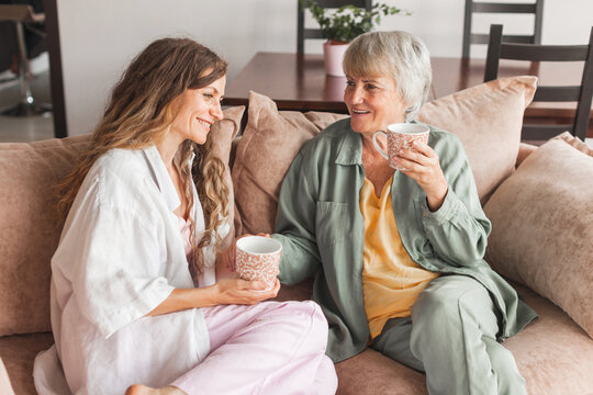 Happy adult daughter and senior mother having fun enjoying talk sit on sofa at home