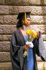 A you black woman wearing a graduation gown looking excited to be a graduand