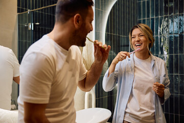 Happy woman and her husband having fun while brushing teeth.