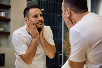 Obraz premium Reflection in mirror of mid adult man looking at his face.