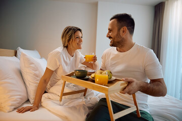 Happy woman talking to her husband who is serving her breakfast in bed.