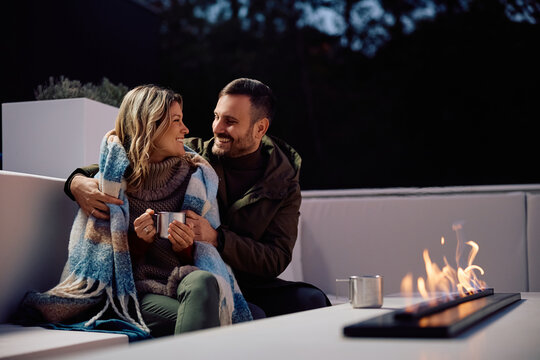 Happy couple talking while enjoying in chilly night by fireplace on  terrace. Copy space.