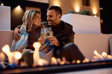 Happy couple toasting while relaxing by fireplace on terrace in evening.