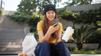 Gen Z eco go green woman asia sit happy relax at tree public park city life enjoy typing mobile...