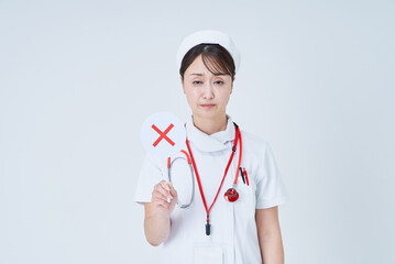 バツが書かれたプレートを持つ白衣姿の女性