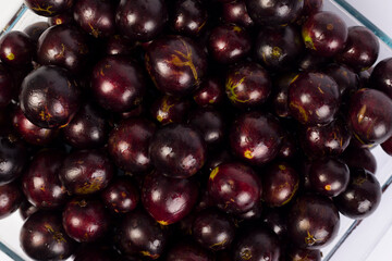 transparent Bowl full of Brazilian fruit jabuticabas on a white background