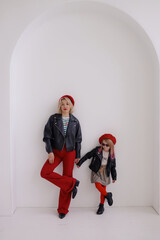 A woman and a girl are standing against the wall, holding hands.